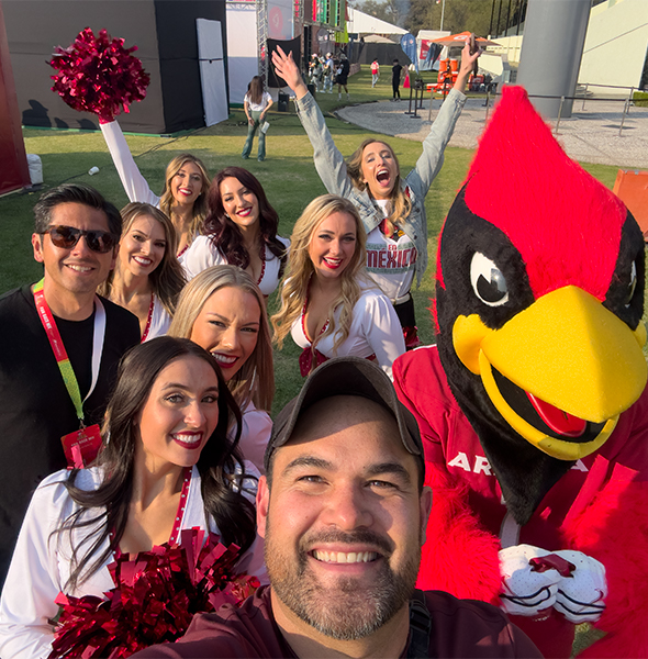 Fotografía del equipo Piso 8 sonriendo junto a botarga de un cardenal en un campo